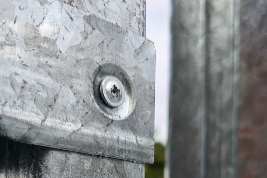 Pormenor macro de dois perfis em aço galvanizado unidos por parafuso
              autoperfurante, com a textura da galvanização à vista.